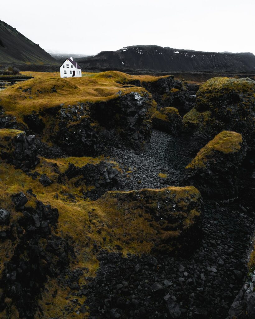 Solitary white house on rugged rocks in mossy valley with distant dark mountains landscape wallpaper