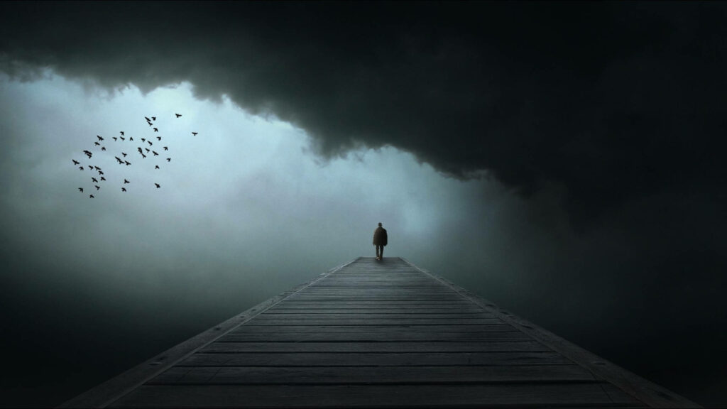 Isolated Soul Standing in Solitude on Desolate Bridge Surrounded by Eerie Mist and Clouds, Birds Whip through Gloomy Sky Wallpaper