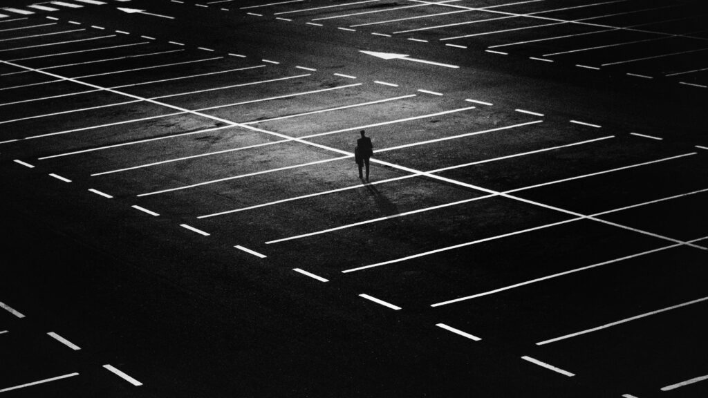 Solitude in Monochrome: A Man Standing Alone on a Dark Parking Lot Wallpaper