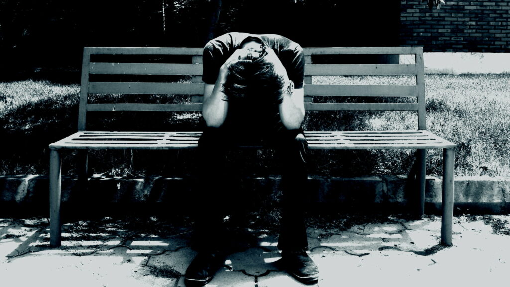 Solitude's Embrace: A Heartbreaking Portrait of a Depressed Man Sitting on a Wooden Bench against a QHD Wallpaper Background