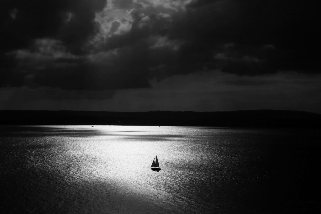 Solitude and Serenity: A Captivating Image of a Black Sailboat Embracing the Tranquil Seas Against a Dramatic Sky Backdrop Wallpaper