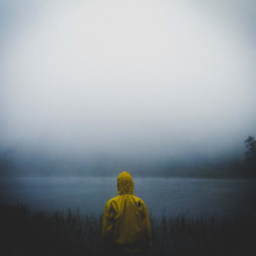 Lost in Solitude: A Lone Figure Donning a Vibrant Yellow Jacket in the Heart of Wilderness Wallpaper