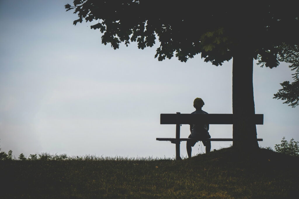 Solitude on a Brown Wooden Bench: A Silhouette of a Lonely Child Against a Wallpaper Background Photo