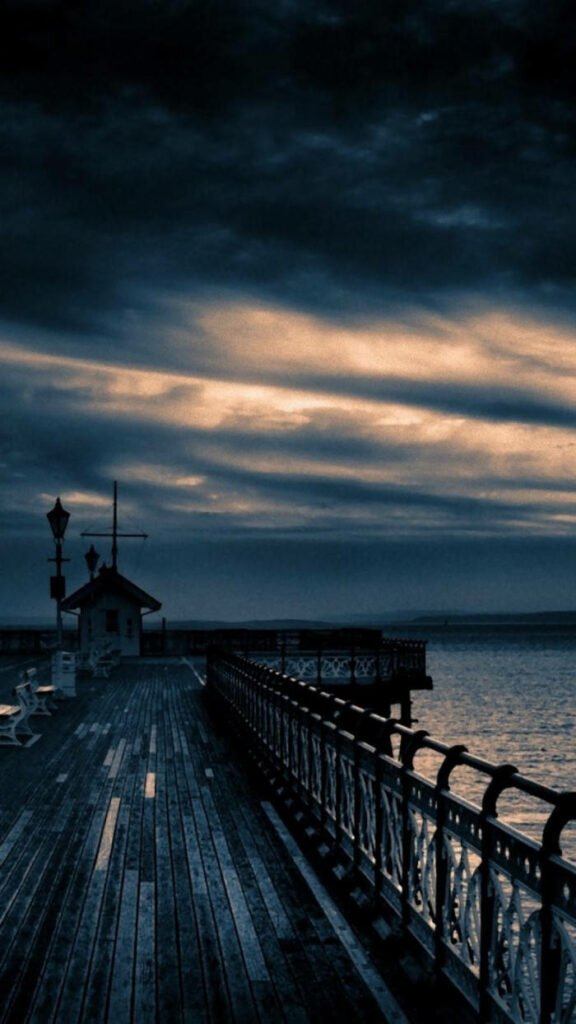 Serene Dusk Beach: Wooden Veranda Over Calm Waters & Moody Sky Wallpaper