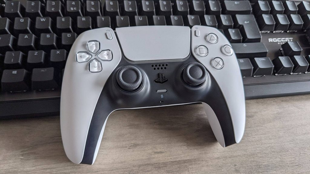 Sony PlayStation 5 DualSense controller on black Roccat keyboard wooden desk gaming setup wallpaper