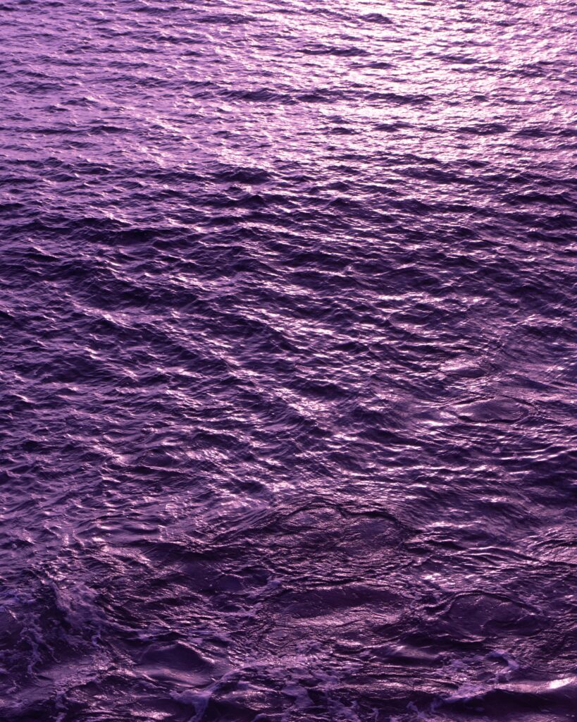 Purple water surface with gentle ripples and glimmering waves creating a serene background Wallpaper
