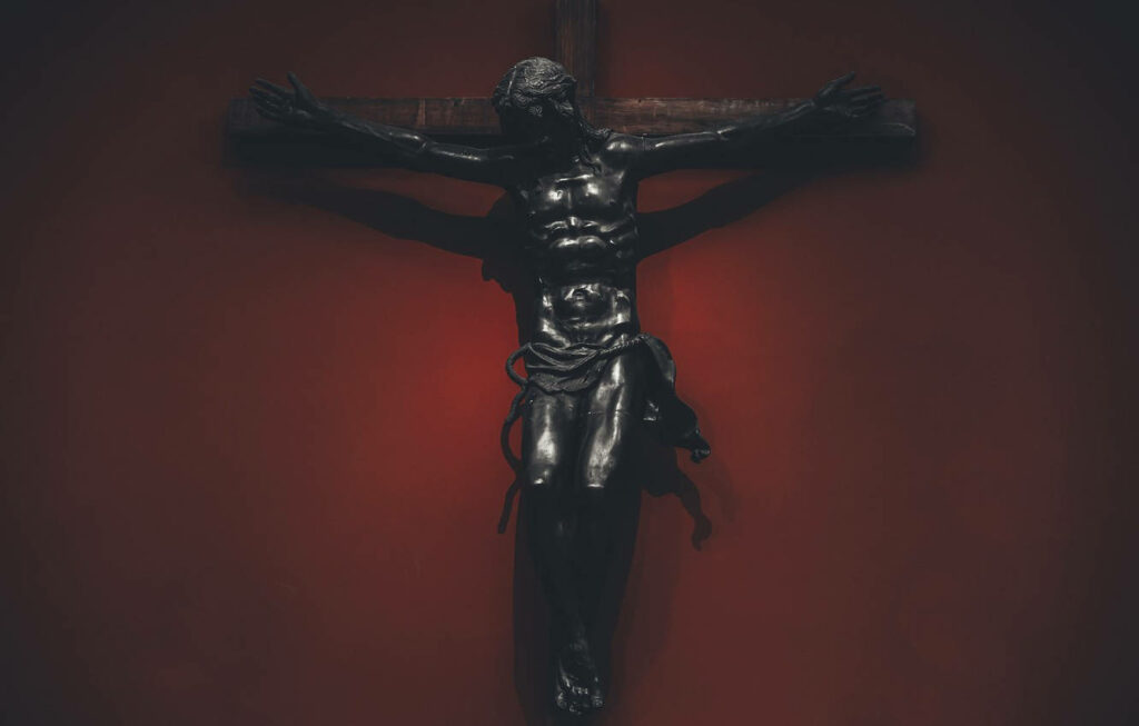 Gloomy Depiction: Jesus Christ Crucified on Mahogany Cross Against a Crimson Backdrop. Perfect Devotional Wallpaper for God-inspired Laptops.
