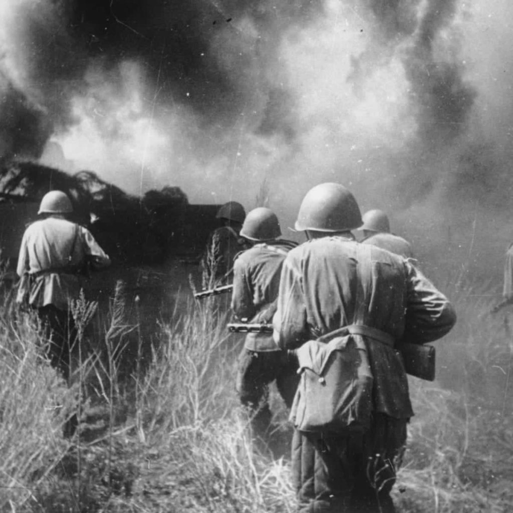Black and white WWII Soviet soldiers advancing through tall grass on burning Eastern Front battlefield Wallpaper