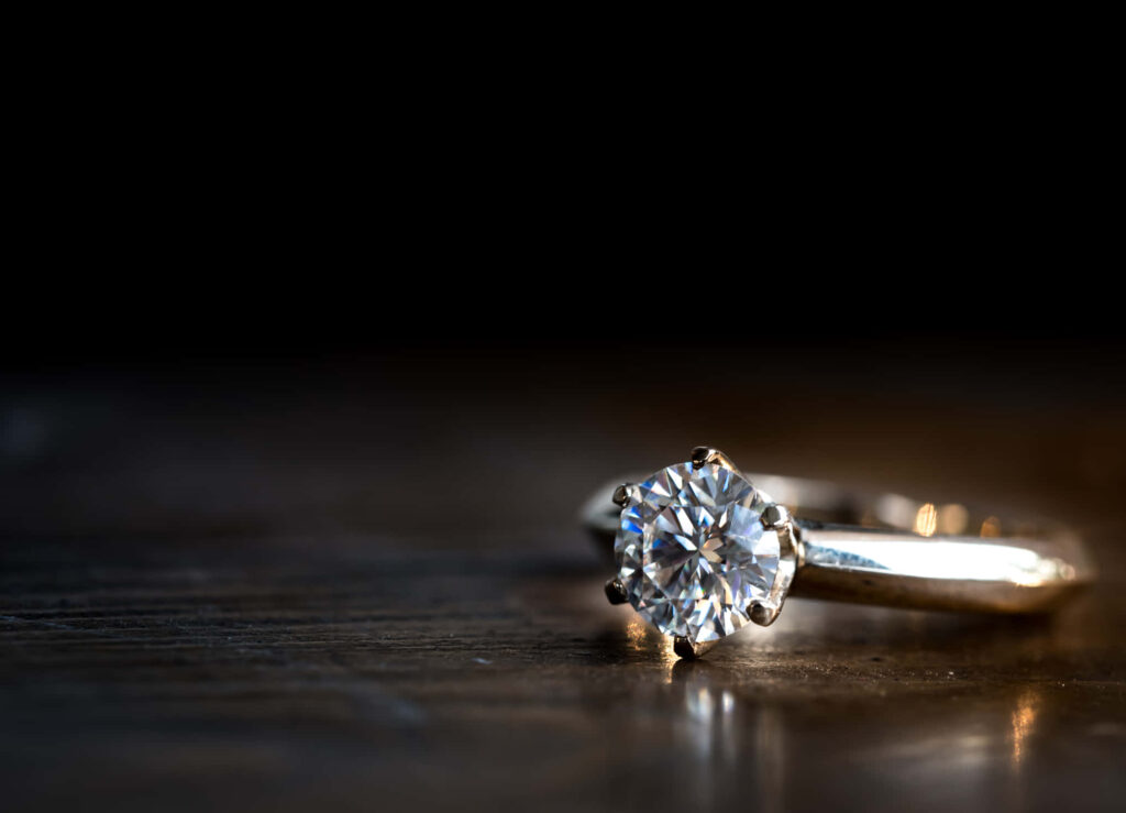 Close-up of sparkling diamond engagement ring on silver band with dark blurred background wallpaper