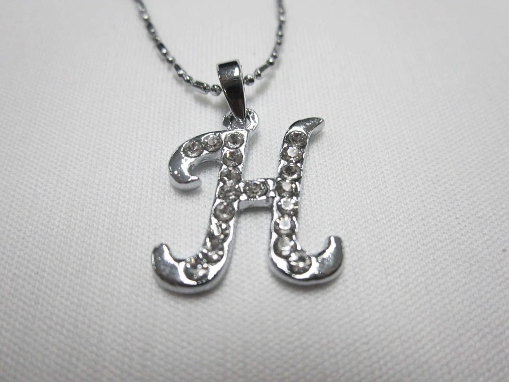 Close-up of silver H pendant with clear crystals on delicate ball chain on soft off-white background Wallpaper