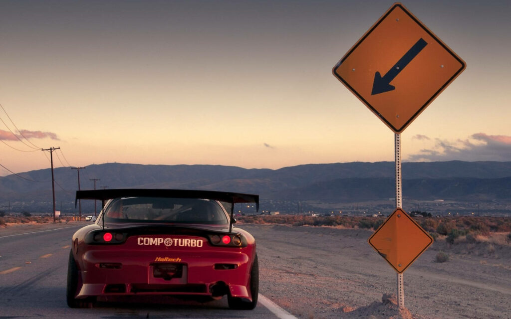 Roaring Through Solitude: A Striking Red Mazda Rx-7 Dominates an Empty Highway, Embracing Speed amidst Serene Mountaintops Wallpaper