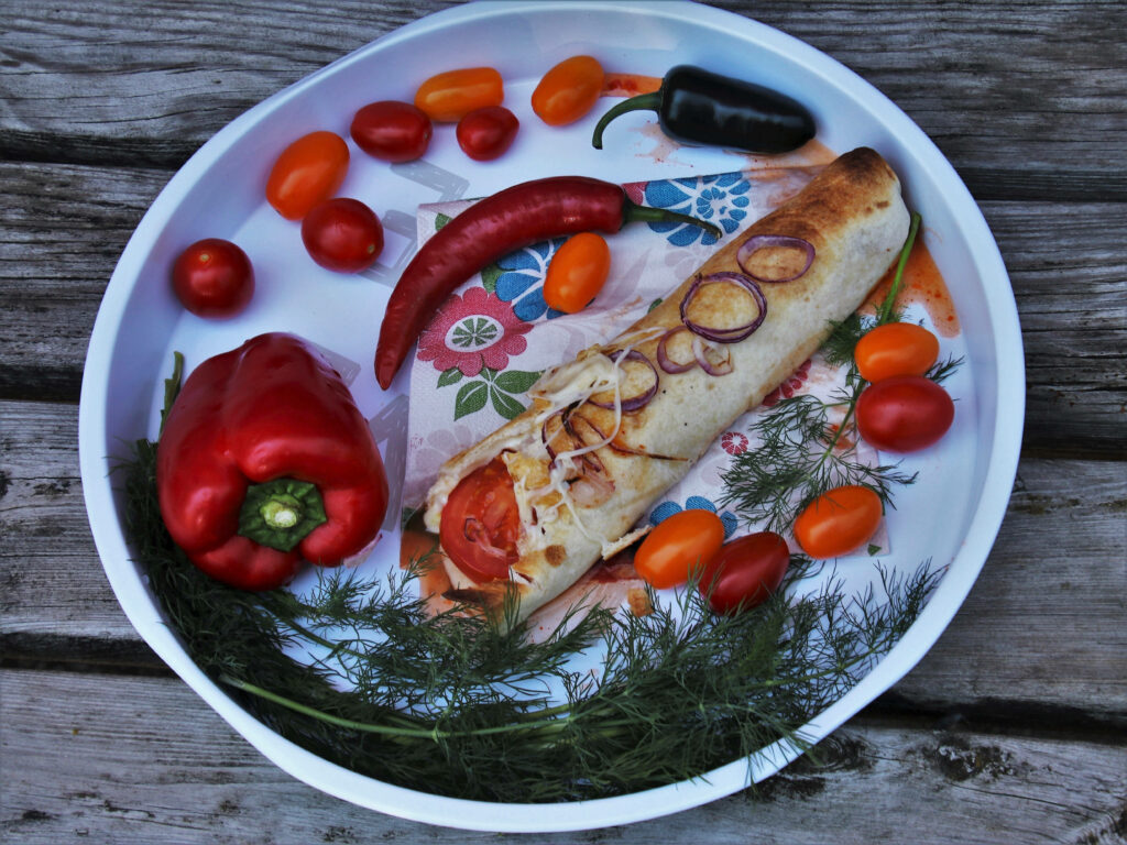 Spicy chili burrito with cheese red onion cherry tomatoes bell pepper and dill on wooden background Wallpaper
