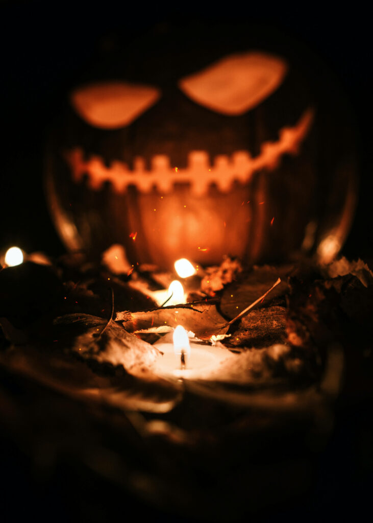 Spooktacular Halloween Vibes - Enchanting Candle and Fiery Pumpkin on Mysterious Dark-Hued Phone Wallpaper
