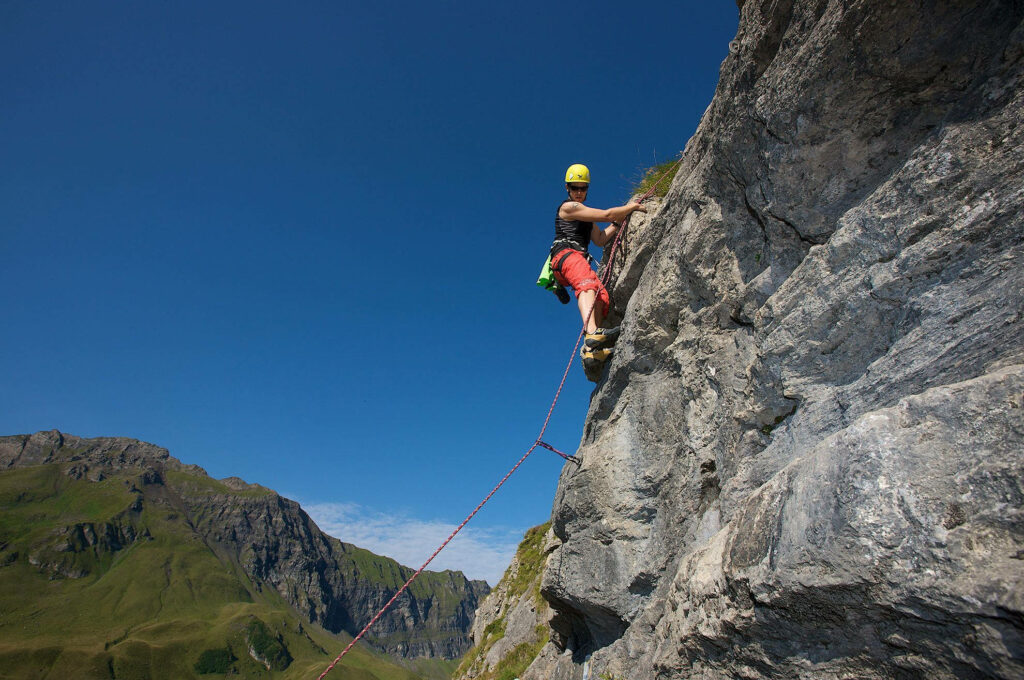 Climber scaling rugged rock face under clear sky alpine scenery Melchsee-Frutt Swiss mountains Wallpaper