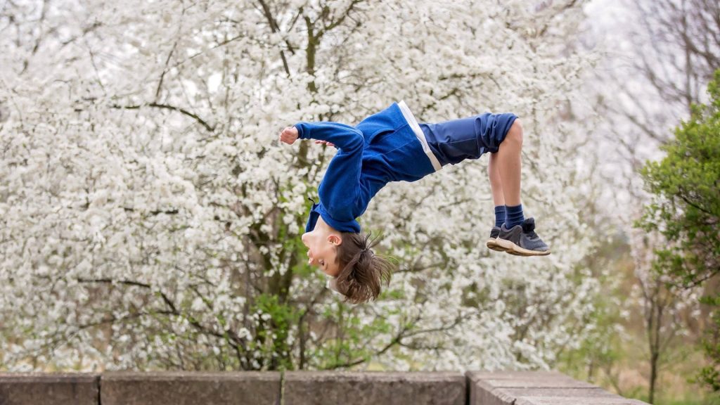 Young boy in blue outfit doing backflip under white blossom tree vibrant spring wallpaper