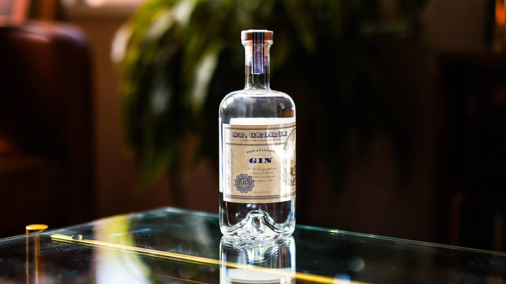 St George Botanivore Gin bottle on reflective glass table with lush green natural background Wallpaper