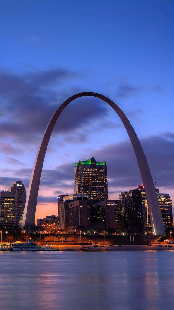 St Louis skyline at twilight with illuminated Gateway Arch and colorful sunset over Mississippi River Wallpaper