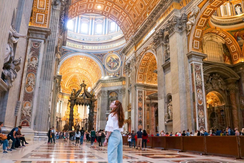 Woman admiring golden Renaissance interior and vaulted ceilings of St Peters Basilica Vatican City Wallpaper