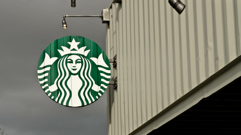 Starbucks logo sign on building exterior under cloudy sky modern inviting coffee shop facade Wallpaper