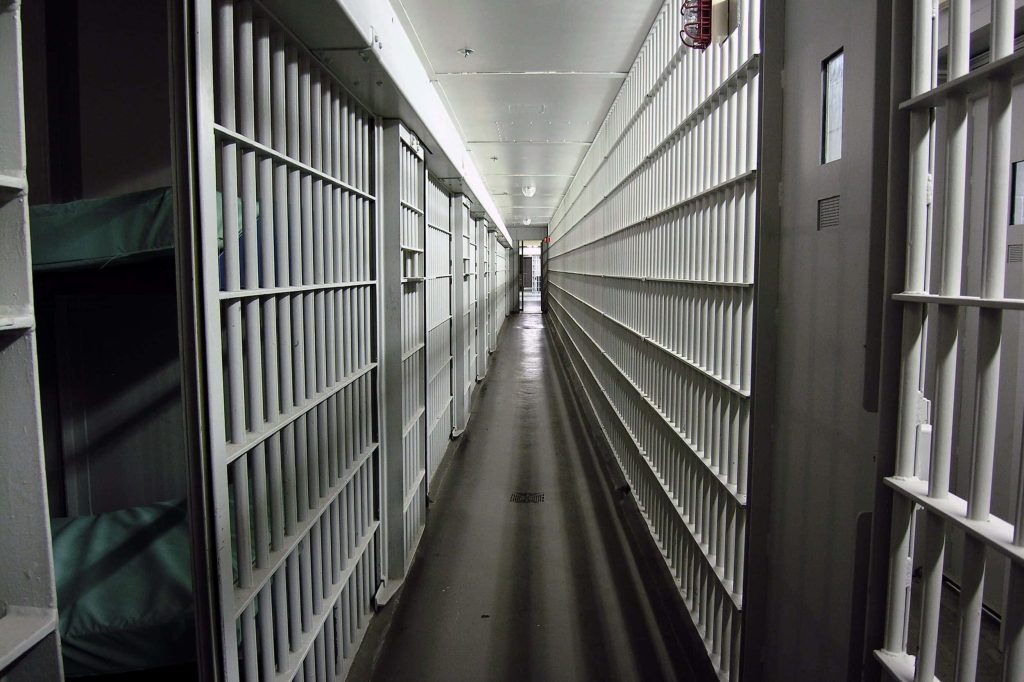 Long clinical prison corridor with heavy steel bars stark cold lighting minimalist jail wallpaper