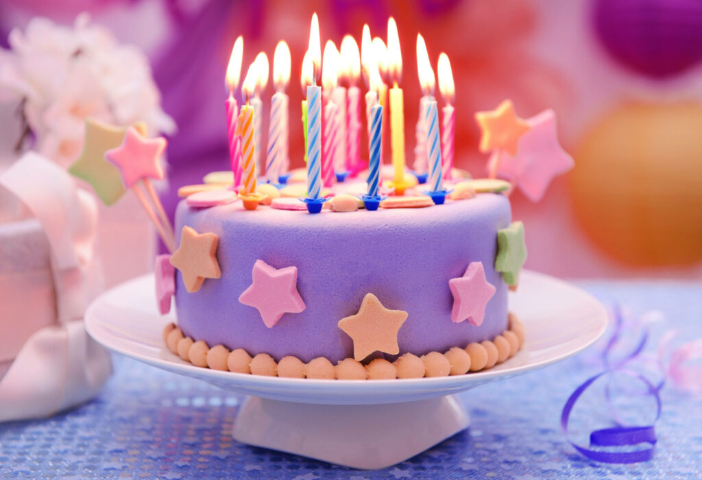 Stellar Celebration: Vibrant Pastel Birthday Cake Illuminated with Glowing Candles, Adorned with Playful Stars Wallpaper