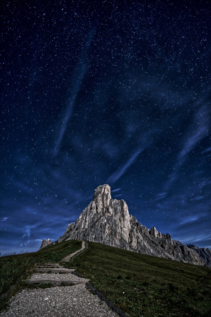Winding path to rugged mountain peak under starry night sky with clouds serene landscape wallpaper
