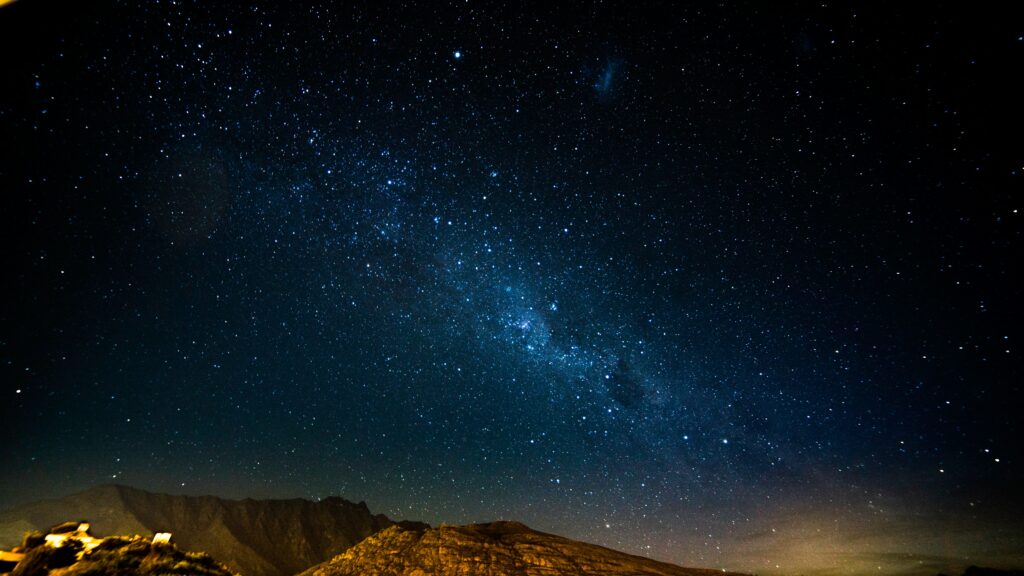 Starry night sky over rugged mountains with glittering stars and serene glowing landscape wallpaper