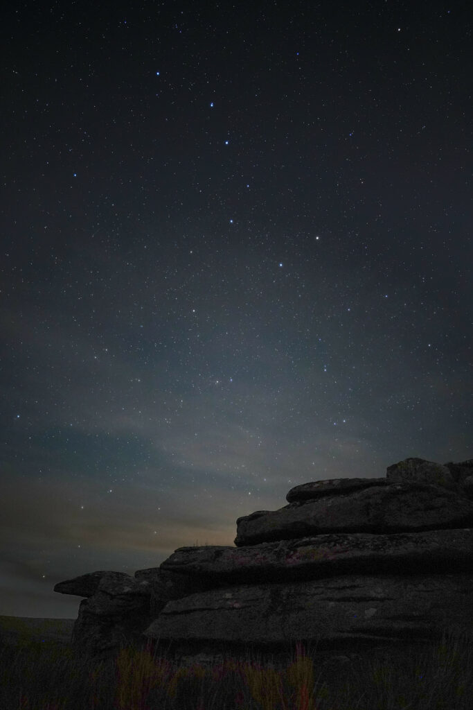 Rugged stones on grass under a vast starry night sky with deep blues and serene natural textures Wallpaper