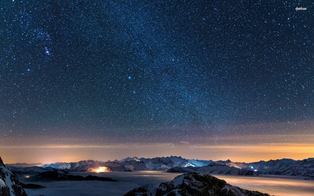 Starry sky over snow-capped mountains with misty valleys and glowing horizon wallpaper background