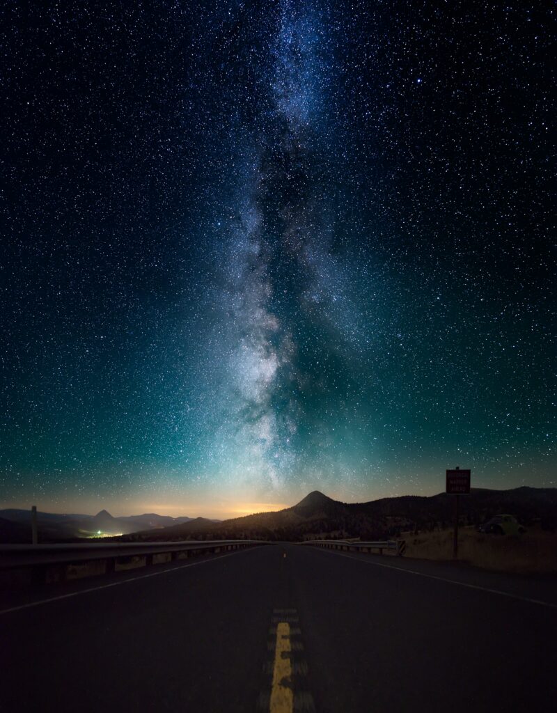 Quiet road under vibrant starry night sky with glowing Milky Way and distant hill lights Wallpaper