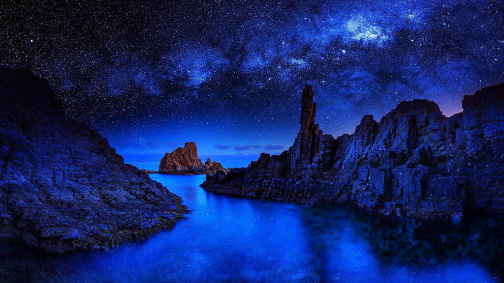 Starry Seascape: A Reflection on the Dark Water and Landscape with HD Wallpaper of Stunning Stars and Rock Formation