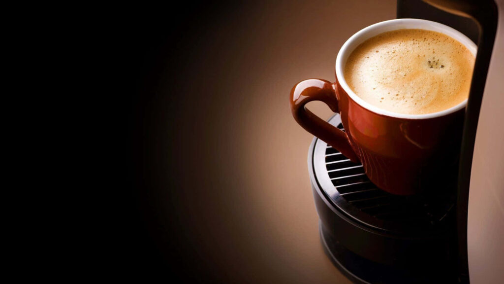Steaming cup of rich black coffee on machine with warm soft light perfect morning start wallpaper