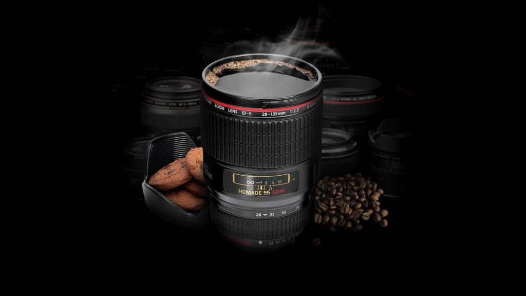 Steaming black coffee in camera lens mug with coffee beans and biscuits background wallpaper