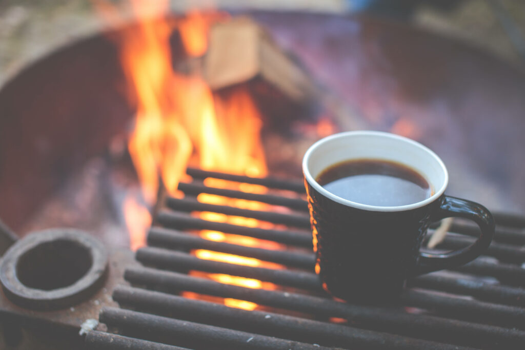 Steaming coffee cup on outdoor fire grill with warm flames and rustic nature setting wallpaper