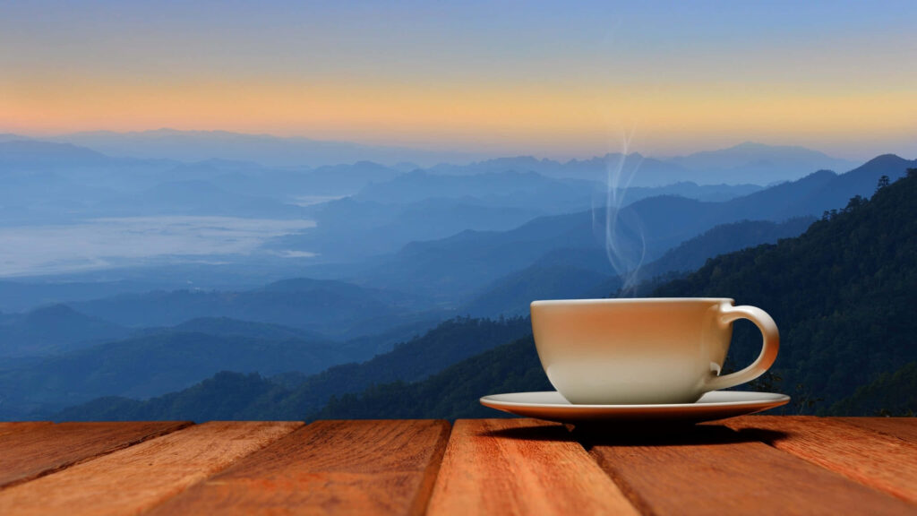 Steaming coffee cup on wooden table with layered mountains and colorful sunrise sky background Wallpaper