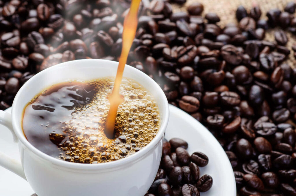 Steaming cup of fresh coffee pouring surrounded by glossy beans warm morning energy wallpaper