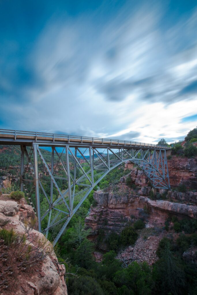 Steel bridge over rocky cliffs with lush greenery and mountains under dramatic cloudy sky wallpaper