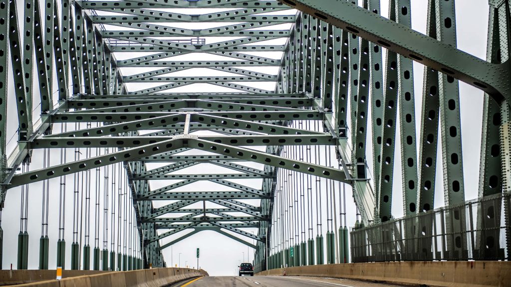 Symmetrical steel truss bridge with lone car framed by green metalwork in moody industrial scene Wallpaper
