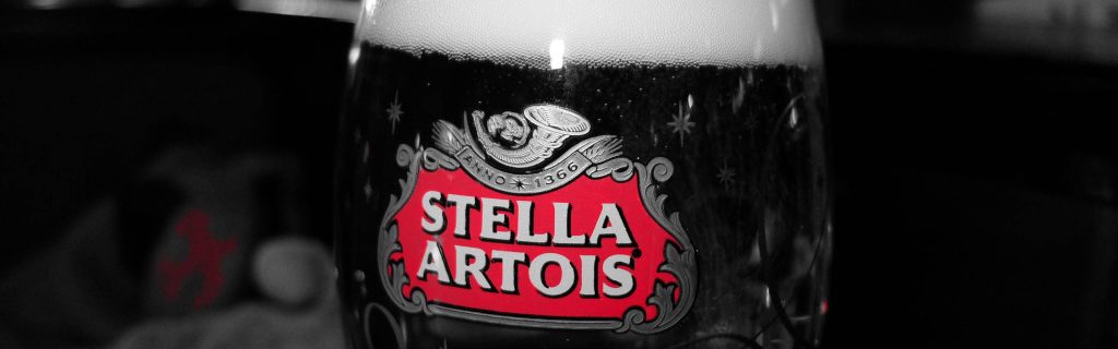 Close-up of Stella Artois beer glass with iconic red white logo on black and white background Wallpaper