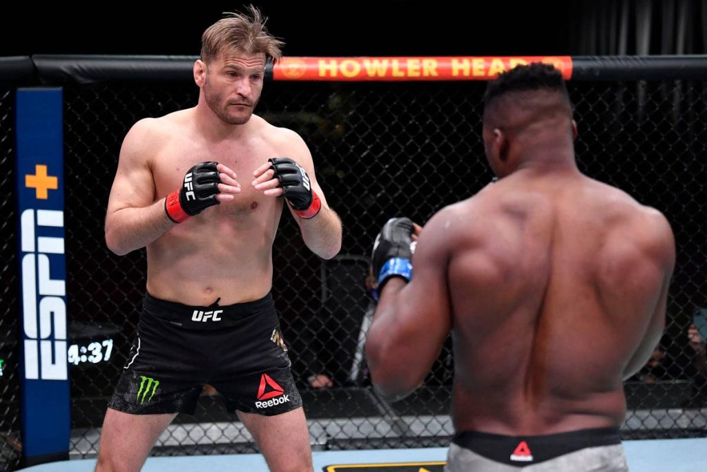 Stipe Miocic in poised UFC octagon stance seen over Francis Ngannou shoulder intense MMA wallpaper