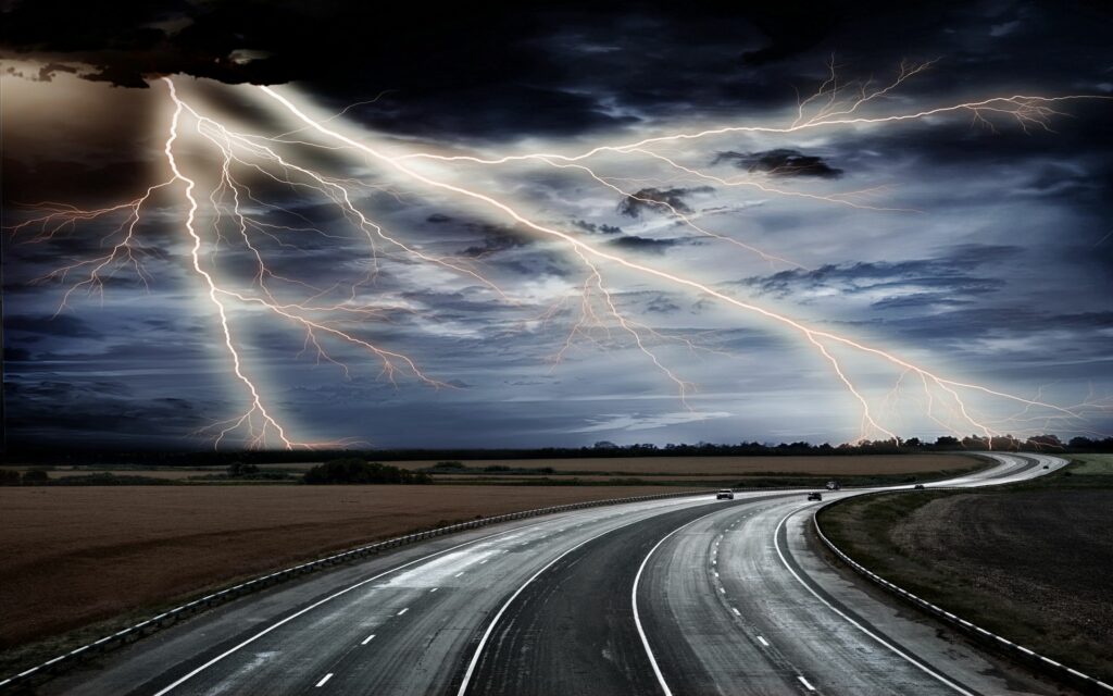 Stormy sky with lightning over winding wet asphalt road and cars driving dynamic weather wallpaper