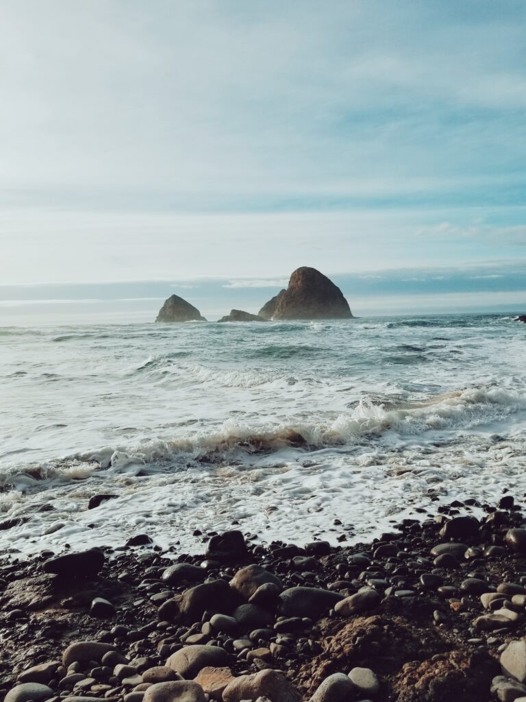 Dramatic coastal scene with rugged rocks waves stormy sky pebbled beach deep blue grey tones Wallpaper