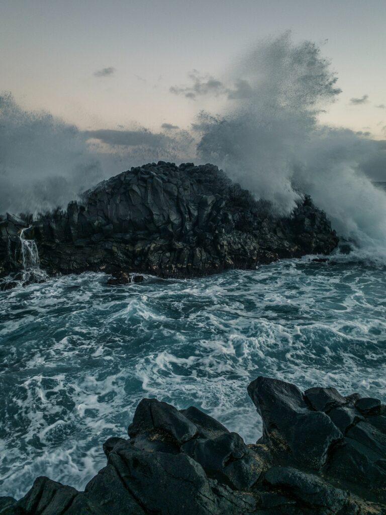 Stormy coastal waves crash on rugged black rocks with dramatic water spray and deep blue sea Wallpaper