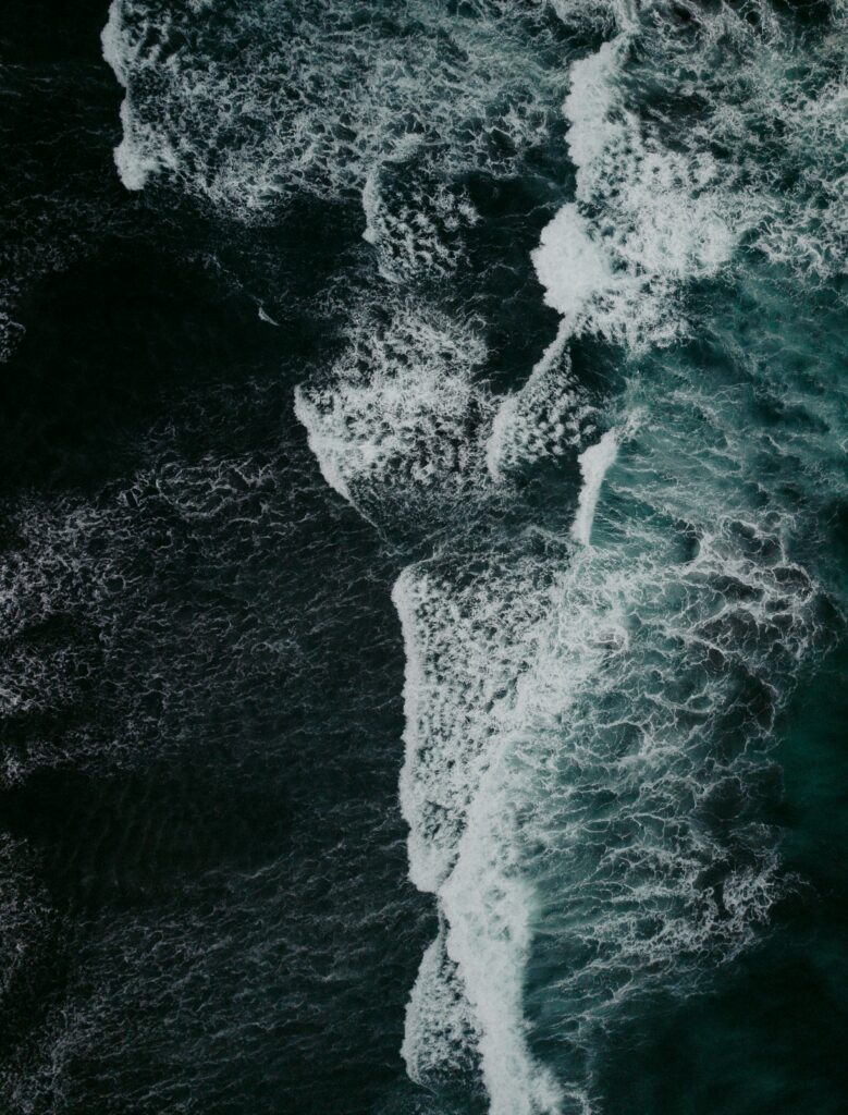 Aerial view of powerful ocean waves crashing on shore with deep blue turquoise and white foam Wallpaper