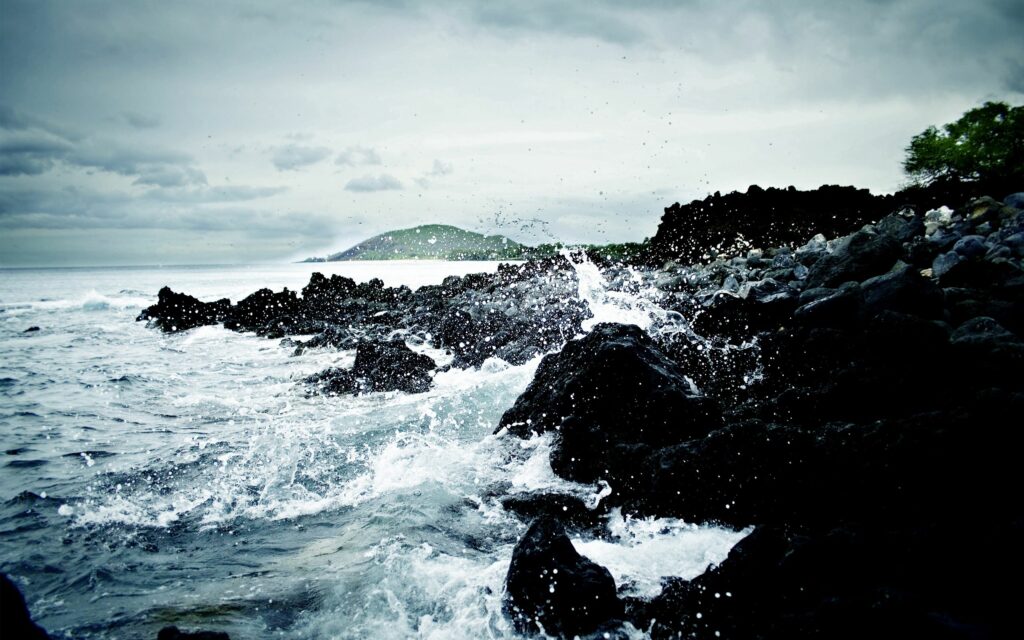 Ocean waves crashing on jagged dark stones under stormy sky with dramatic splashes wallpaper background