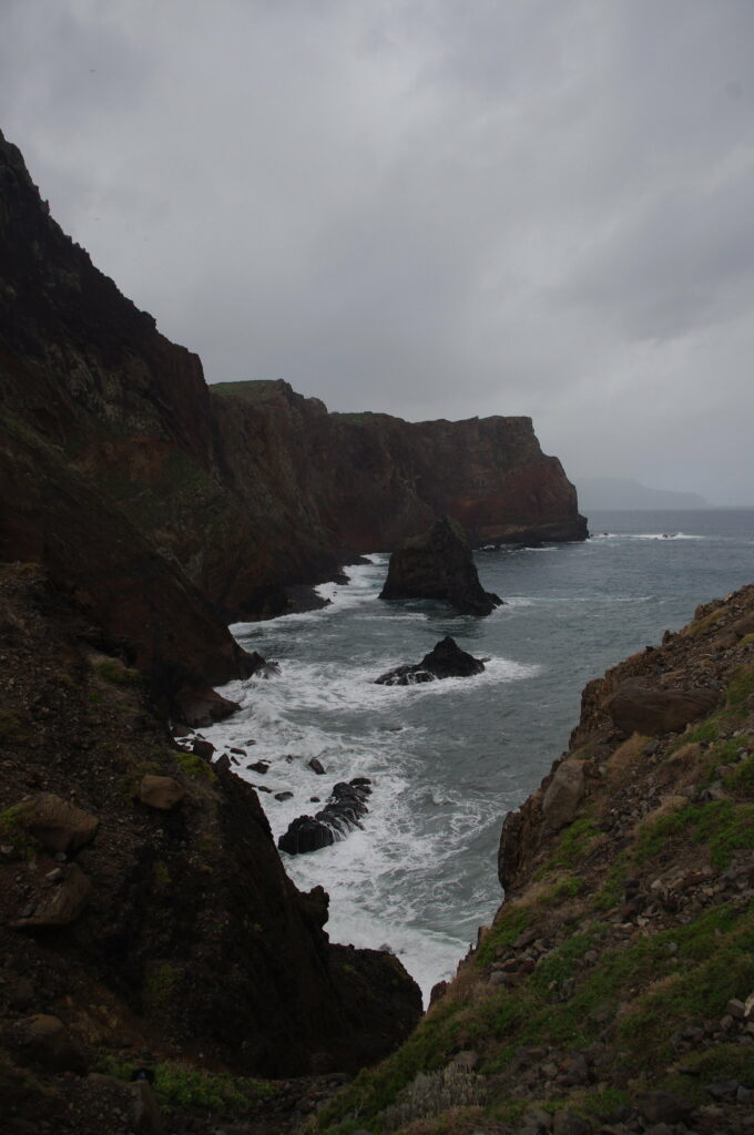 Stormy sea crashing against rugged cliffs under moody overcast sky wild coastal landscape Wallpaper