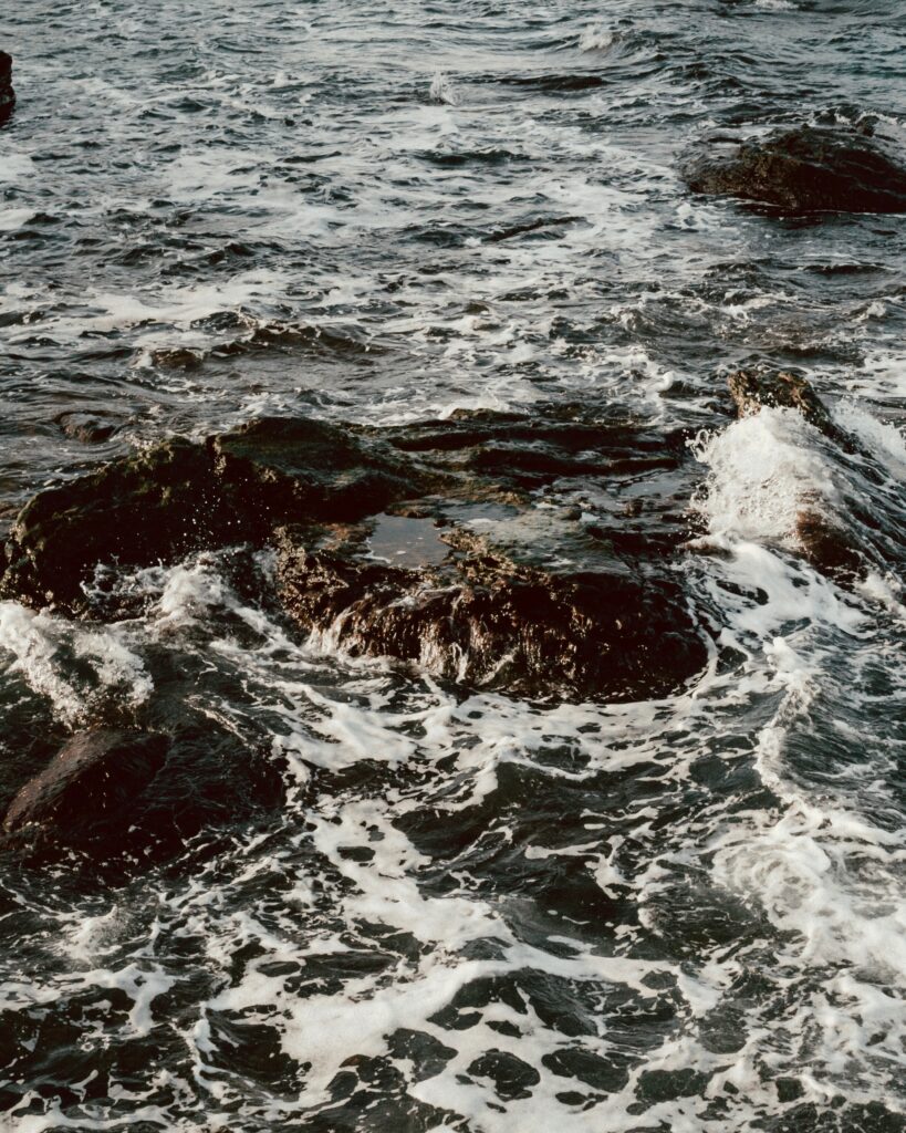 Stormy sea crashing waves over rugged stones foamy water deep blue and earthy tones wallpaper