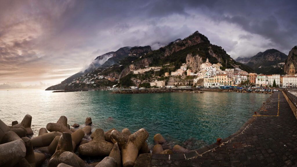 Stormy sky over Amalfi Coast colorful cliffside buildings turquoise sea scenic coastal view Wallpaper