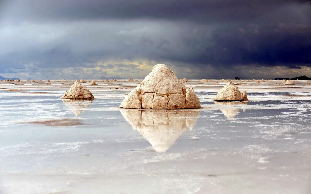Reflective lake with pyramid stone and salt formations under stormy skies dramatic landscape wallpaper