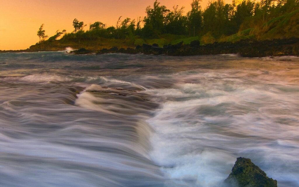 Dynamic waves crashing on rugged coast under stormy sunset sky with blending warm cool tones Wallpaper